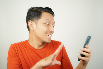 Asian man in orange t-shirt happy looking at what's on smartphone on isolated background