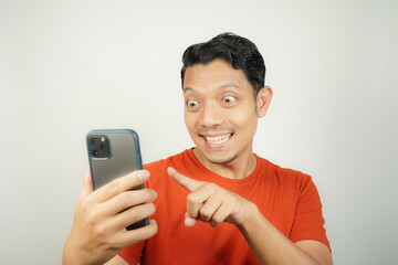 Asian man in orange t-shirt smiling happily looking at smartphone on isolated background