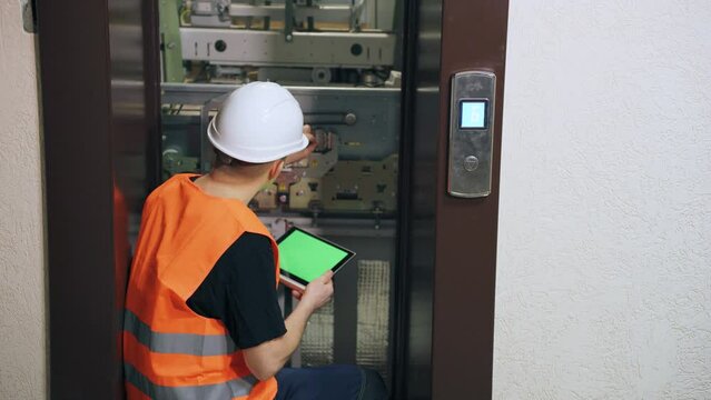 A male elevator repairman enters data on the operation of equipment into a digital tablet. Inventory of elevator equipment parts, performance check.