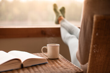 person at home relaxing reading a book enjoying a hot morning cup of tea 