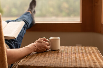 Person at home relaxing with feet up by the window reading and enjoying a morning cup of coffee 