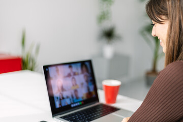 Young woman studying online at home. Rear view of millennial female listening on laptop video call. Education or business concept.