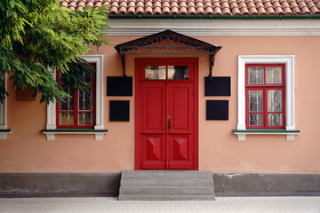 Urban building facade featuring a red door, ornate windows, and green foliage, exhibiting classic architectural charm