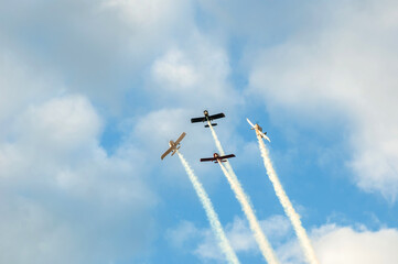 Four planes performing synchronized maneuvers with smoke trails streaking across the sky and clouds