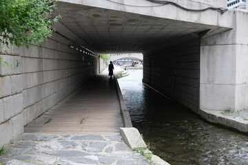 Person walking under a bridge along a stream in Seoul, South Korea