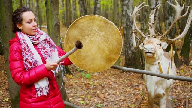 Woman beats tambourine near stuffed deer in forest at autumn day