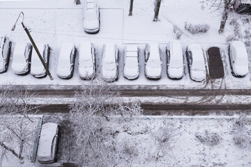 Many Cars and road under snow on a street parking after snowfall and blizzard. Car covered snow top view, cold snowy weather