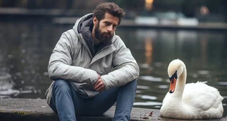 Foto op Aluminium handsome bearded man in winter jacket sitting near lake with swan © YannTouvay