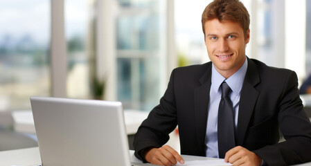 Fototapeta premium Handsome businessman sitting at desk in office and working on laptop