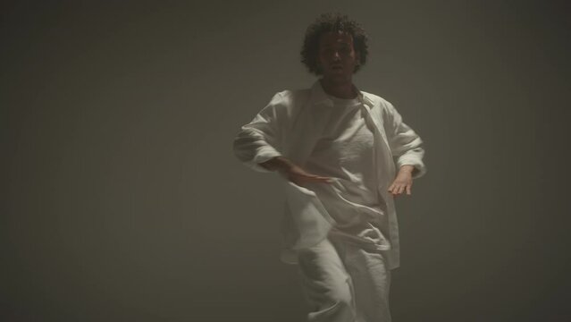 Tilt down shot of young male dancer in white suit dancing barefoot in studio with cyc wall