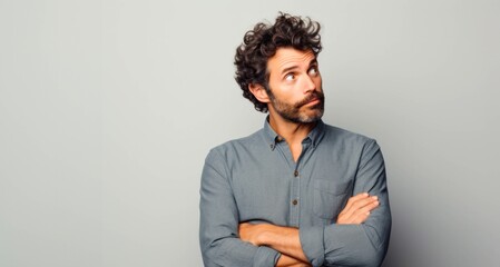 Handsome man with curly hair looking up and thinking on grey background