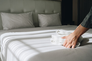 Cropped shot view of hotel maid hands arranging towels on bed in hotel bedroom.