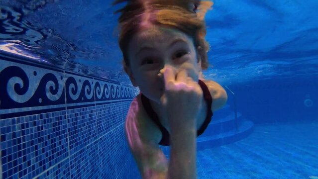 Cute little girl dives in the pool holding her nose. Family moments, joy, swimming pool. 