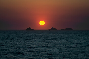 Fototapeta premium Red sunset dusk sky view saw from Arpoador rock (Pedra do Arpoador) with Tijucas islands in sight on the horizon under summer afternoon sunny clear sky in Ipanema district in Rio de Janeiro - Brazil.