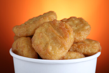 Bucket with delicious chicken nuggets on orange background, closeup