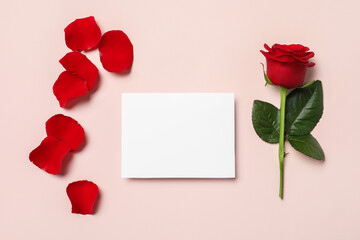 Blank card, beautiful red rose and petals on pale pink background, flat lay. Space for text