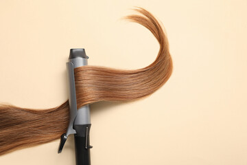 Curling iron with hair lock on beige background, top view. Space for text