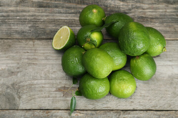 Pile of fresh wet limes and leaves on wooden table, top view. Space for text