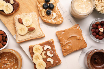 Toasts with different nut butters, fruits and nuts on white marble table, flat lay