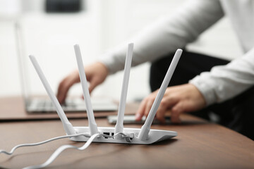 Man with laptop and smartphone working at wooden table, focus on Wi-Fi router