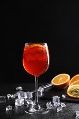 Glass of tasty Aperol spritz cocktail with orange slices and ice cubes on table against black background