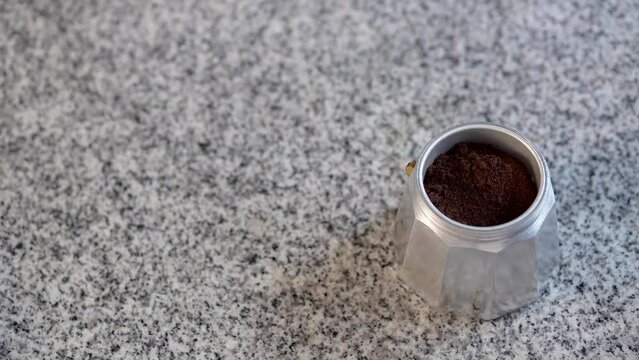 preparado de cafe en cafetera italiana poniendo cargas de cafe molido en polvo sobre mesa de textura granito