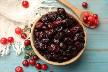 Tasty dried cranberries in bowl and fresh ones on light blue wooden table, top view