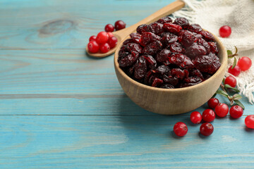 Tasty dried cranberries in bowl and fresh ones on light blue wooden table. Space for text