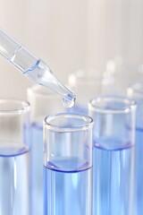 Laboratory analysis. Dripping light blue liquid from pipette into glass test tube on blurred background, closeup
