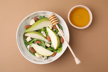 Delicious pear salad in bowl, honey and dipper on beige background, top view