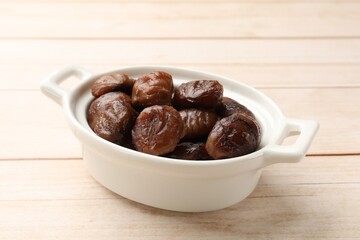 Roasted edible sweet chestnuts in dish on light wooden table