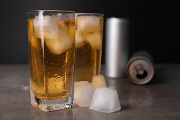 Tasty energy drink with ice cubes in glasses and aluminium cans on grey table, closeup