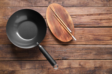 Empty iron wok and chopsticks on wooden table, flat lay. Space for text