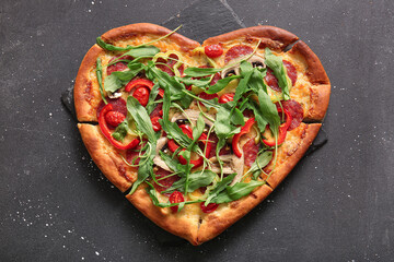 Board with tasty heart shaped pizza on black background