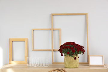 Bouquet of chrysanthemum flowers, blank frames and word HOME on wooden table in living room