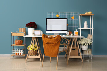 Interior of stylish home office with comfortable workplace, chrysanthemum flowers and pumpkins