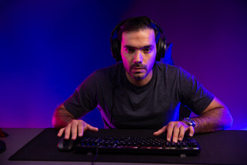 Smart gaming streamer concentrating gaming players trying to pass the level at mission completed, using headset and mic for communicate others on streaming live at neon lighting studio room. Surmise.