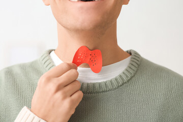 Young man with paper thyroid gland at home, closeup