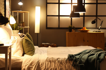 Interior of modern bedroom with blankets on comfortable bed and glowing lamps at night