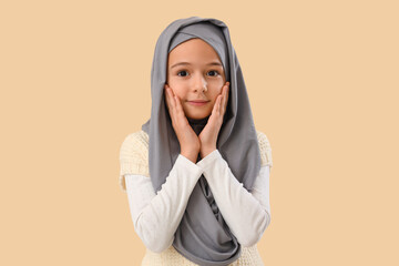 Little Muslim girl in hijab on beige background