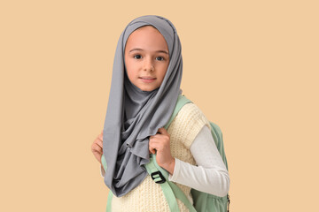 Little Muslim girl in hijab with school backpack on beige background