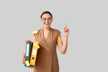 Young businesswoman in eyeglasses with document folders pointing at something on light background