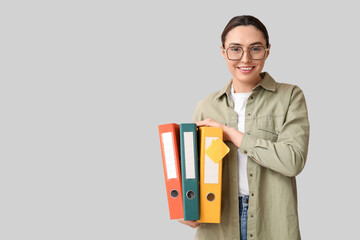 Young businesswoman in eyeglasses with document folders on light background