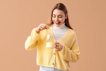 Young woman dipping tea bag into cup on beige background