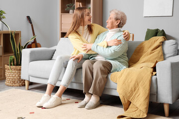 Young woman hugging her grandmother on sofa at home