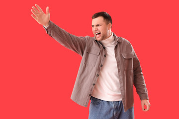 Angry young man shouting on red background. Accusation concept