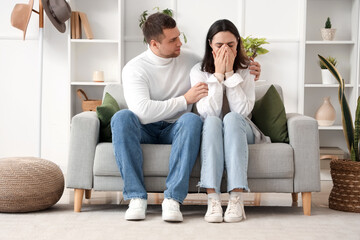 Young man hugging his crying wife on sofa at home