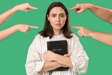 People pointing at young woman with Holy Bible on green background. Accusation concept