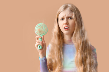 Young woman with hair loss problem and brush on beige background