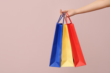 Female hand with paper shopping bags on light background. Valentine's Day celebration